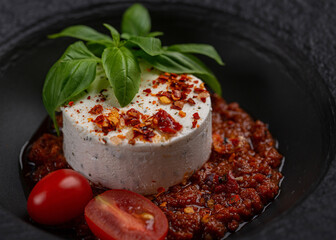 a portion of goat cheese with basil, pesto sauce and tomatoes in a large black dish,