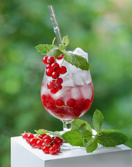 cold refreshing fruit drink with red currant berries in a transparent glass flute with ice, with...