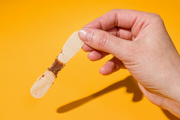 used wooden popsicle ice cream stick in hand on yellow background