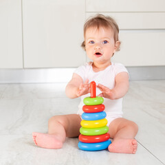 Adorable baby girl playing with colorful pyramid toy