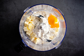 Pastry Dough Ingredients in a Food Processor Bowl: Flour, butter, powdered sugar, and egg yolk in a...