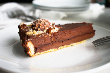 Slice of Chocolate Hazelnut Tart Garnished with Chocolates and Nuts: Chocolate ganache tart garnished with candy and chopped nuts