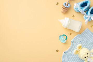 Baby accessories concept. Top view vertical photo of blue shirt knitted booties milk bottle wooden rattle soother knitted bunny toy and gold stars on isolated pastel beige background with empty space