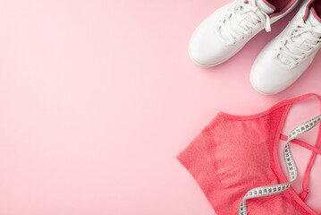 Fitness concept. Top view photo of white sneakers pink sports bra and tape measure on isolated pastel pink background with copyspace