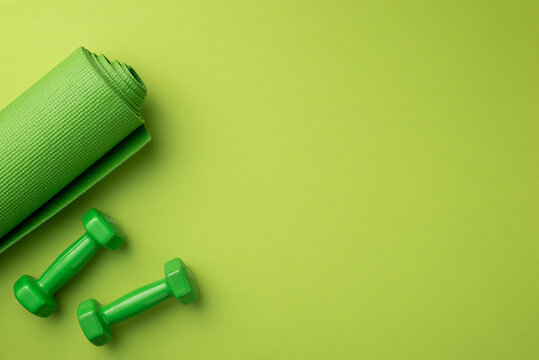 Sports concept. Top view photo of green exercise mat and dumbbells on isolated green background with empty space