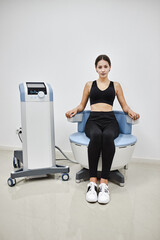Young woman sitting on electromagnetic chair for stimulation of deep pelvic floor muscles and...