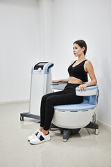 Young woman sitting on electromagnetic chair for stimulation of deep pelvic floor muscles and restoring neuromuscular control at the clinic