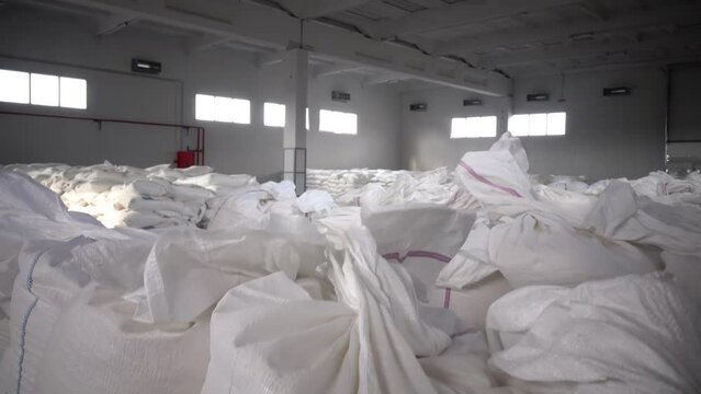 White sacks with flour, sugar, groats or pasta in a production warehouse. Storage of packaged goods in the warehouse. Bagful on wooden pallets, packed products stored in a large bright storage room.
