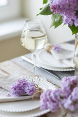 Beautiful table decor for a wedding dinner with a spring blooming lilac flowers. Celebration of a special event. Fancy white plates, wineglasses. Countryside style