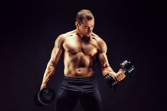 Powerful man doing the exercises with dumbbells. Photo of young man with good physique isolated on black background. 