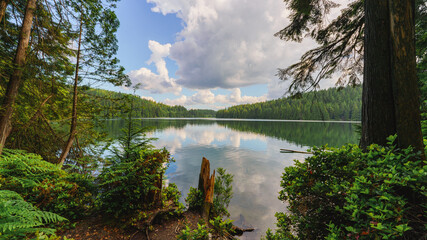Clouds reflected on tranquil Sasamat Lake, Belcarra Regional Park, BC, as seen from Sasamat Loop...