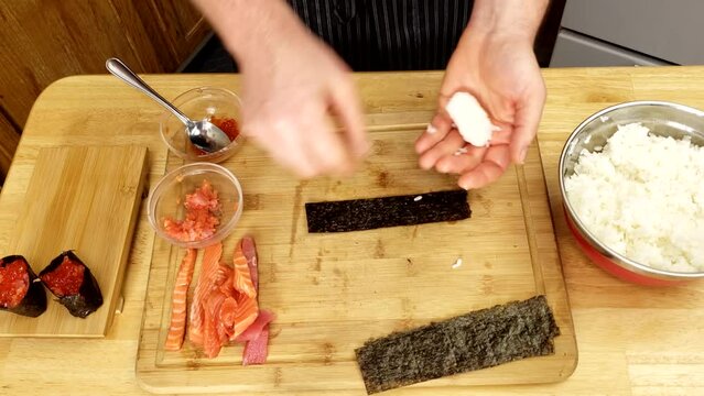 Shaping portion of rice and wrapping it with edible seaweed making battleship sushi container for caviar and quill yolk.