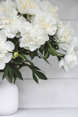 Naklejka na ściany i meble Beautiful white bouquet of peonies in a white vase on a white wooden background. Close-up. Flowers and buds.