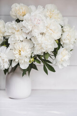 Obraz na płótnie Canvas Beautiful white bouquet of peonies in a white vase on a white wooden background. Close-up. Flowers and buds.