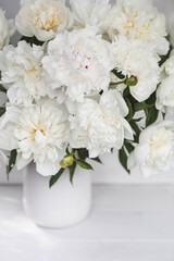 Beautiful white bouquet of peonies in a white vase on a white wooden background. Close-up. Flowers...