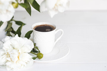 A beautiful postcard. A white coffee cup with a saucer, candles and a vase with a bouquet of white peonies. Beautiful still life. Spring, summer time. The concept of 