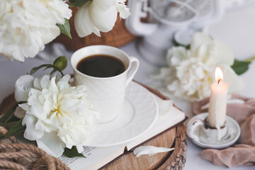 A beautiful postcard. A white coffee cup with a saucer, candles and a vase with a bouquet of white peonies. Beautiful still life. Spring, summer time. The concept of 