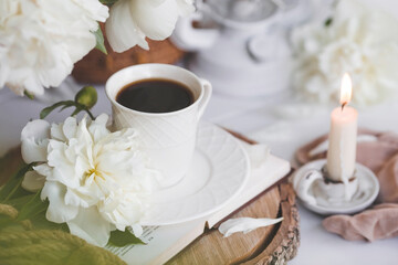 Fototapeta na wymiar A beautiful postcard. A white coffee cup with a saucer, candles and a vase with a bouquet of white peonies. Beautiful still life. Spring, summer time. The concept of 