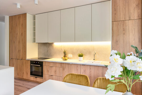 Modern interior of kitchen with stylish furniture with wooden cabinets and dining room with contemporary rable with mustard chairs. Luxury and architecture of indoors.
