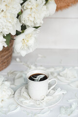 A beautiful postcard. A white coffee cup with a saucer, candles and a vase with a bouquet of white peonies. Beautiful still life. Spring, summer time. The concept of 