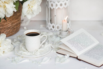 A beautiful postcard. A white coffee cup with a saucer, candles and a vase with a bouquet of white peonies. Beautiful still life. Spring, summer time. The concept of 