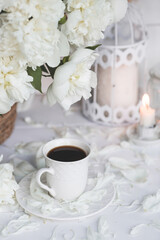 A beautiful postcard. A white coffee cup with a saucer, candles and a vase with a bouquet of white peonies. Beautiful still life. Spring, summer time. The concept of 