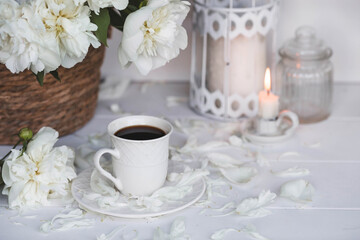 Fototapeta na wymiar A beautiful postcard. A white coffee cup with a saucer, candles and a vase with a bouquet of white peonies. Beautiful still life. Spring, summer time. The concept of 