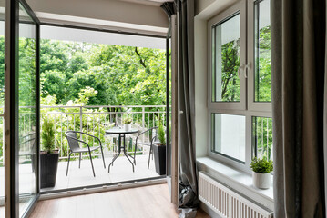 Big balcony window in new apartment with beautiful view on green nature and table with chairs. Modern building with patio.