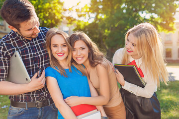
A group of cheerful students near the university building on the lawn with a laptop, books and notebooks