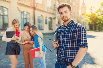 
A group of cheerful students near the university building on the lawn with a laptop, books and notebooks