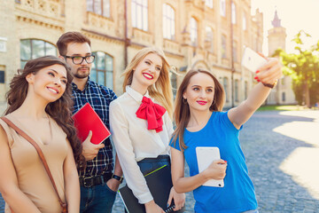 
A group of cheerful students near the university building on the lawn with a laptop, books and notebooks