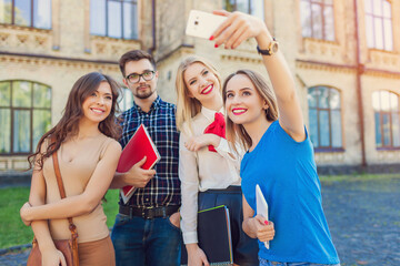 
A group of cheerful students near the university building on the lawn with a laptop, books and notebooks