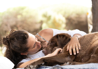 pretty young woman lying in the forest playing with her chocolate Labrador retriever dog