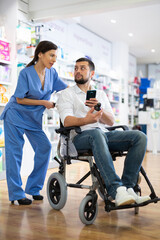 Man in wheelchair consults a woman pharmacist in a pharmacy