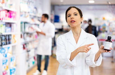 Female druggist standing in salesroom of drugstore and presenting medicine.