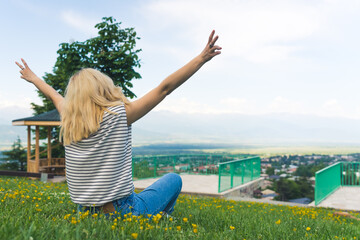 medium shot of a blond girl sitting on the green grass and enjoying a view. High quality photo - Powered by Adobe