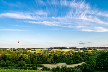 Summer panoramic hilly landscape with fields and forests in Limburg. The hot air balloon flies in the blue sky with white cirrus clouds.