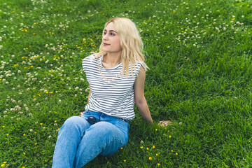 Fototapeta premium blond European girl sitting on the grass and looking up to the sky. medium full shot. High quality photo