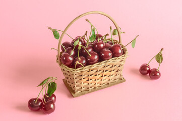 Ripe cherries in a small basket on a pink background in daylight. Selective focus, copy space for text