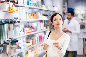 Confident young adult woman consumer holding shopping list shopping at pharmacy