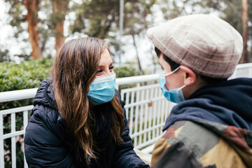 Young blonde latin mother with her young son, using face mask in the park. Single parent family