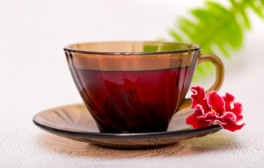 Flower tea karkade. Delicious herbal tropical drink on a bright table. A cup of pink tea from dry hibiscus petals, a natural medicinal drink against the background of fern leaves. Tropical morning.