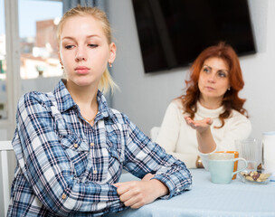 Portrait of sad mature woman trying to talk with daughter in home interior