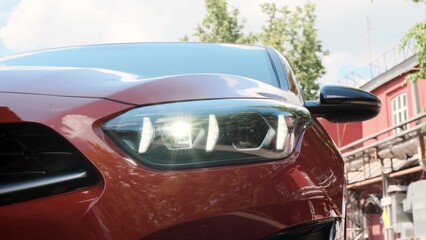 Fototapeta premium close view of front headlight of modern orange colored car. headlight glows with diode lights in new 2022 model car. unrecognizable car is parked in alley.