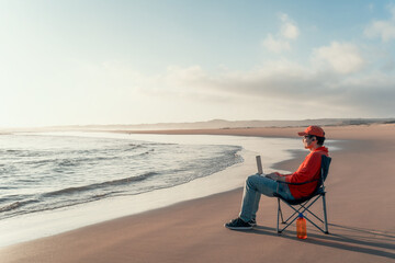 digital nomad sitting on the beach outdoor alone working relaxed and looking at horizon