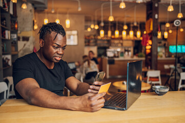 African american man using smartphone and credit card in a cafe