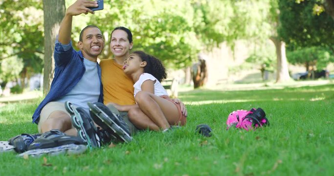 Young carefree family taking a selfie sitting in a park. Cheerful latin man taking a photo with his little daughter and wife in a garden. Playful, parents spending time with their child outside