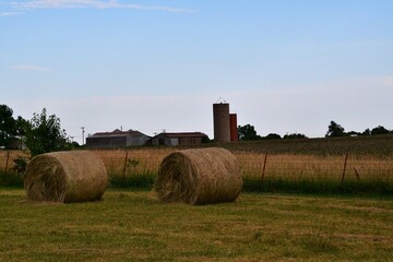 Hay Bales in a Farm Field with Silos and Barns in the Distance