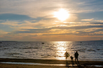 Fototapeta premium A man, woman, and their dog enjoy a beautifully colourful sunset over Lake Nipissing in North Bay, Ontario.