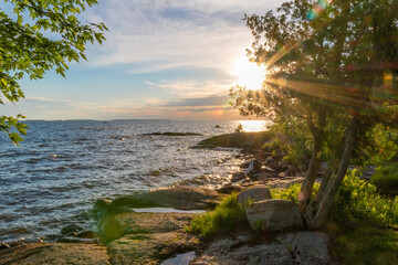 Sun beams poke their way through the lush green leaves of a tree on the shore of Lake Nippising during a beautifully colourful sunset in North Bay, Ontario.